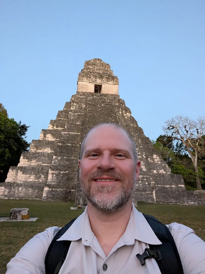 Selfie in front of a tall stepped Maya temple under a clear sky