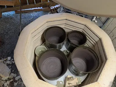 Four large dark brown glazed planters with combed sides inside an open electric kiln