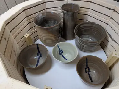 A tall brown vase, a ribbed jar, a ribbed bowl and three bowls with a blue brushed lantern motif inside a kiln
