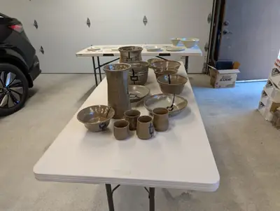 A table of brown stoneware vases, bowls and cups with blue lantern motifs, with celadon plates and bowls on a table behind
