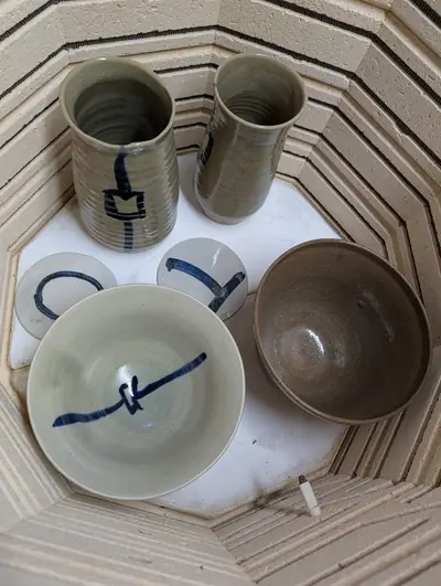 Two crackled green vases, a celadon bowl with a blue lantern, a brown bowl and two round letter tiles inside a kiln