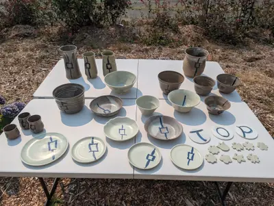 An outdoor table display of lantern-motif vases, bowls, plates and cups, T-O-P letter tiles and small textured ornaments