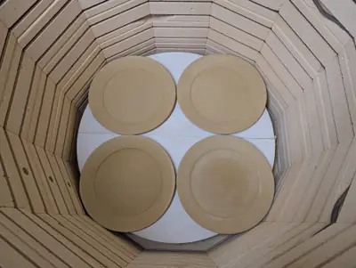 Four unglazed buff dinner plates with wide rims on a kiln shelf, viewed from above