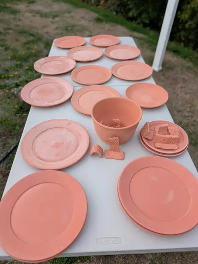 A table of bisque-fired terracotta-colored dinner plates, a planter and small honeycomb-textured pieces outdoors